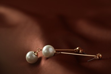 Photo of Beautiful pearl earrings on brown silk, closeup. Space for text