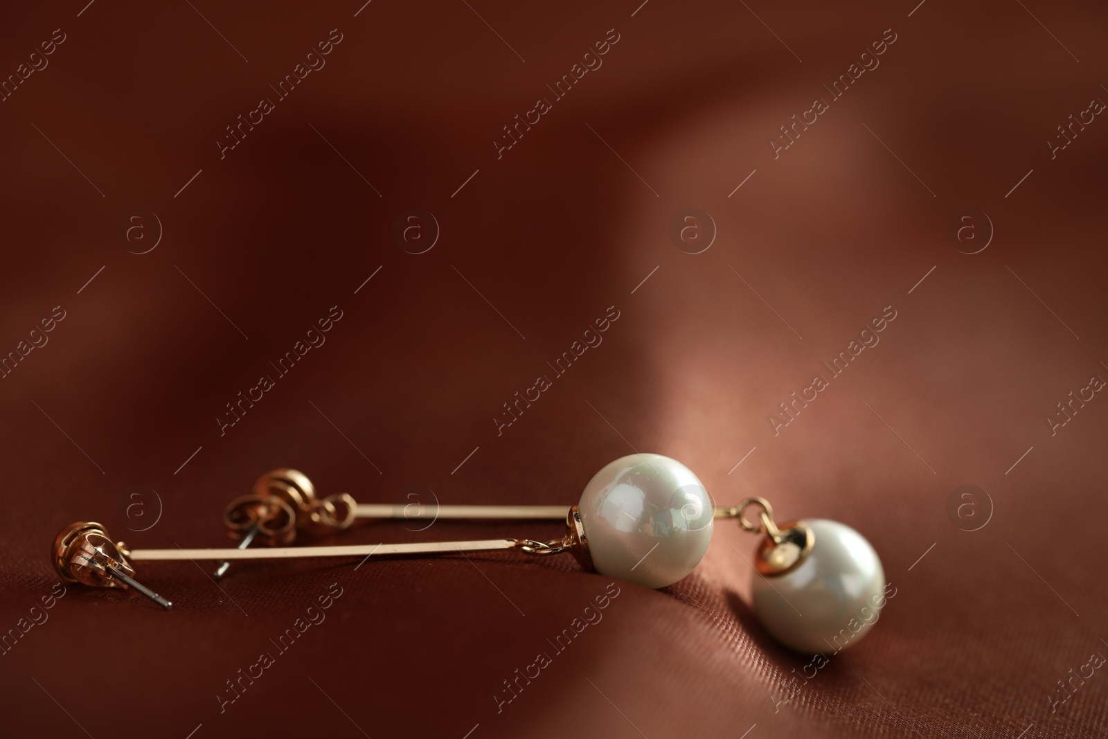 Photo of Beautiful pearl earrings on brown silk, closeup. Space for text