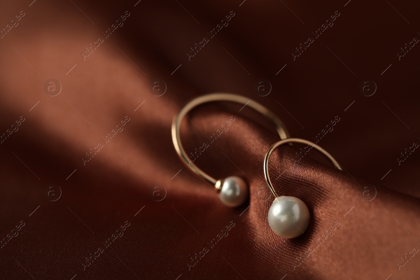 Photo of Beautiful pearl earrings on brown silk, closeup