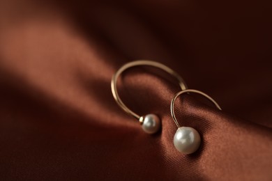 Photo of Beautiful pearl earrings on brown silk, closeup