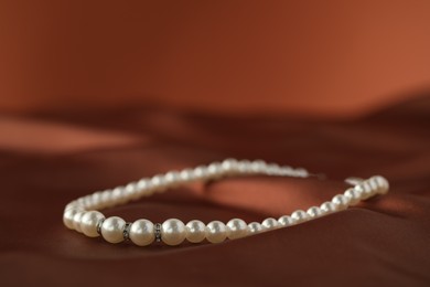 Photo of Beautiful pearl necklace on brown silk, closeup