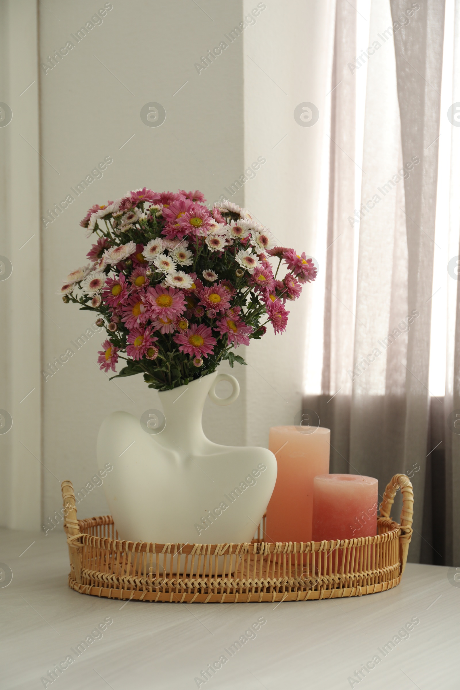 Photo of Stylish vase with beautiful flowers and candles on white wooden table at home