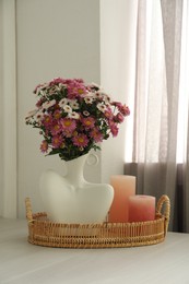 Photo of Stylish vase with beautiful flowers and candles on white wooden table at home