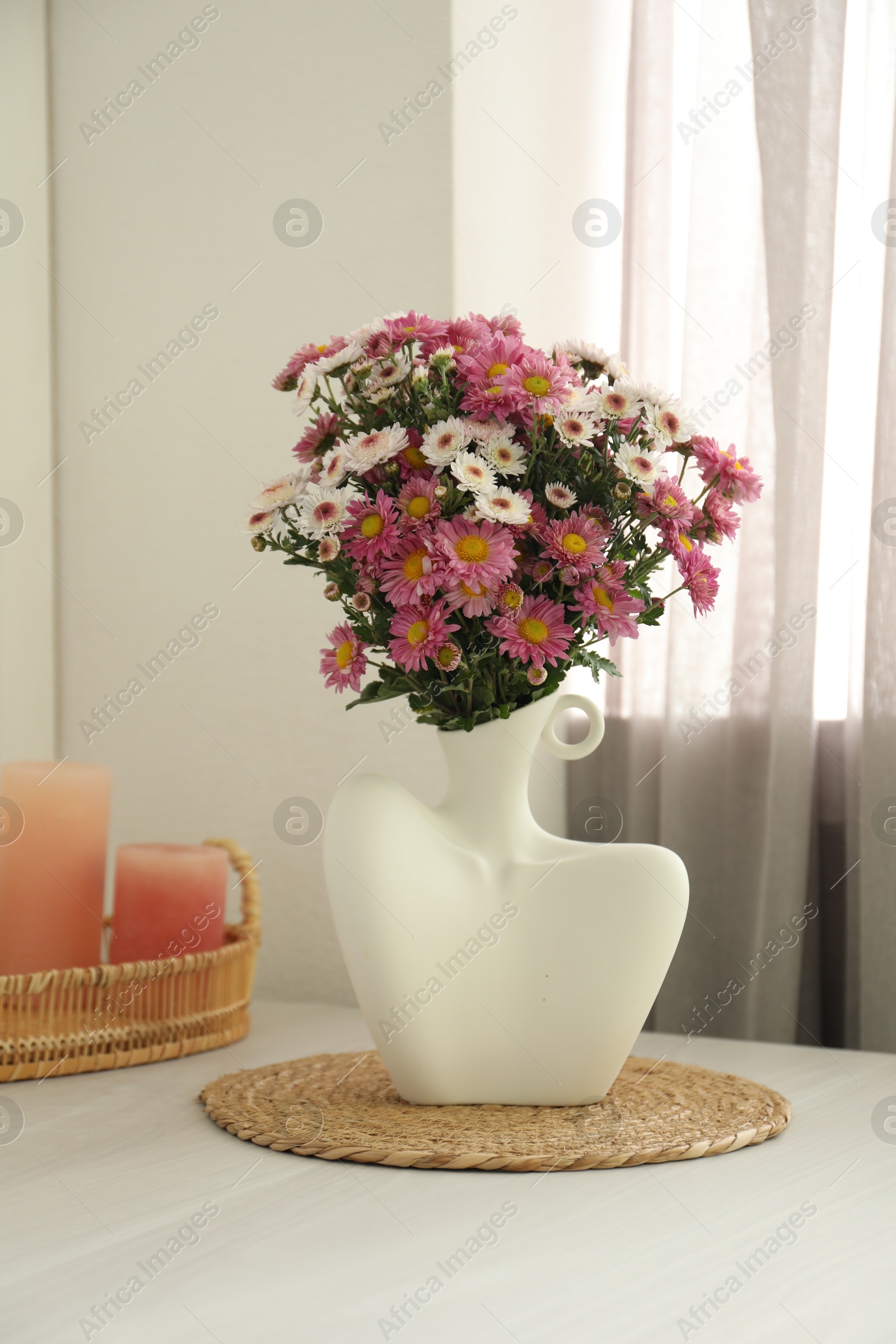 Photo of Stylish vase with beautiful flowers and candles on white wooden table at home