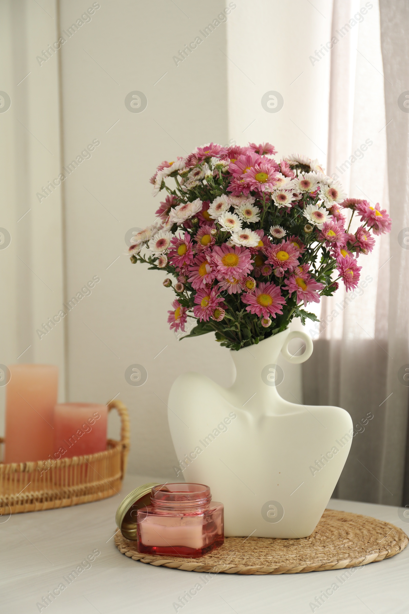 Photo of Stylish vase with beautiful flowers and candles on white wooden table at home