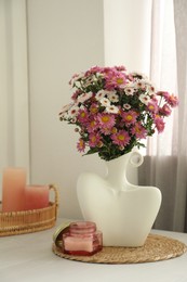 Photo of Stylish vase with beautiful flowers and candles on white wooden table at home