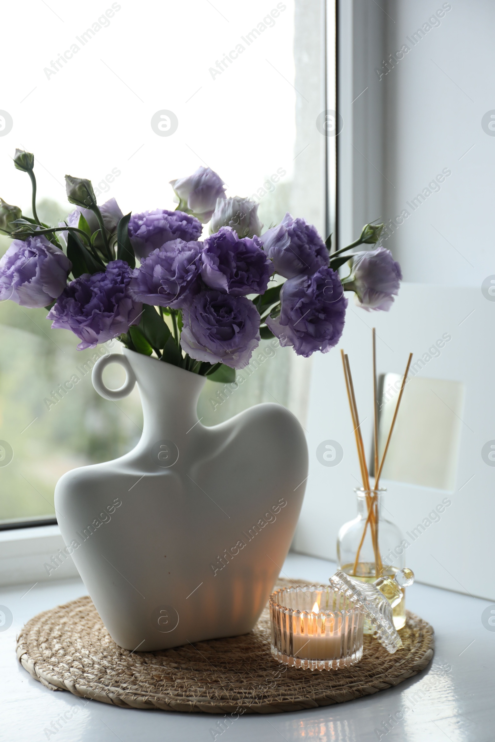 Photo of Stylish vase with beautiful flowers, candle and reed diffuser near window at home