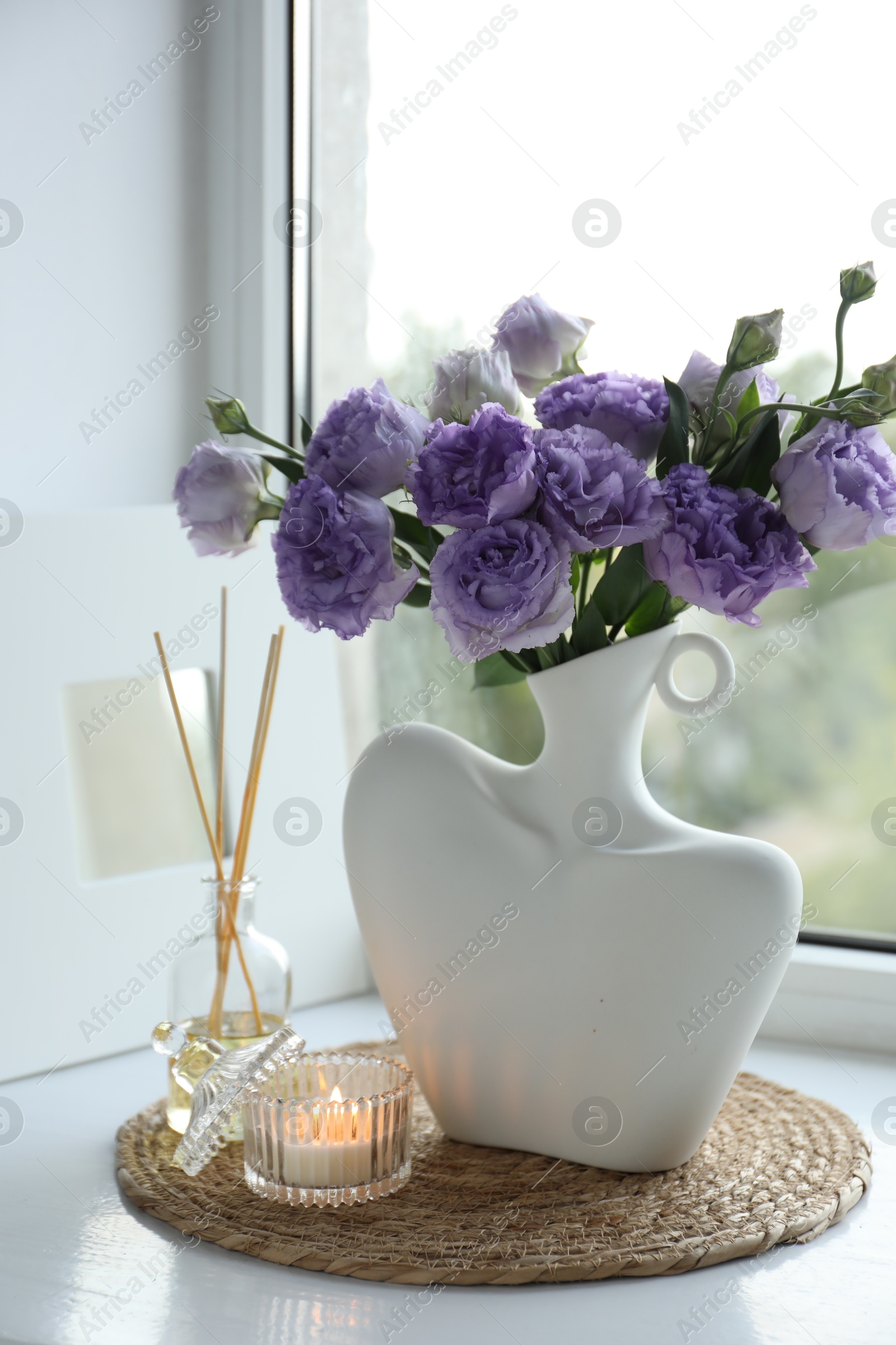 Photo of Stylish vase with beautiful flowers, candle and reed diffuser near window at home