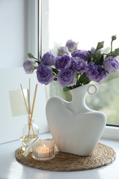 Photo of Stylish vase with beautiful flowers, candle and reed diffuser near window at home