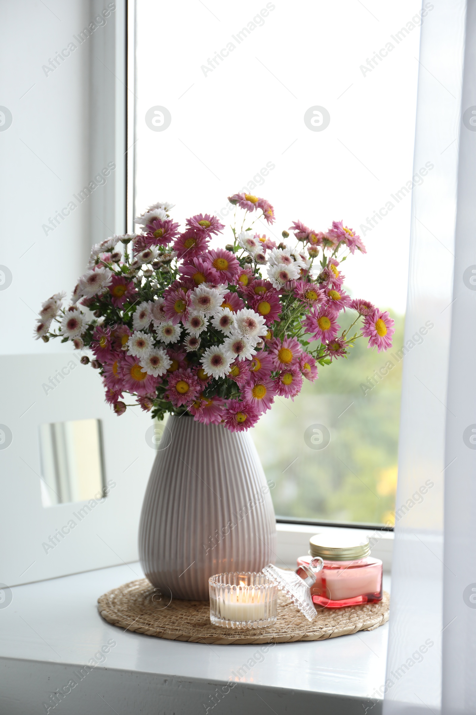 Photo of Beautiful flowers in vase and candles near window at home