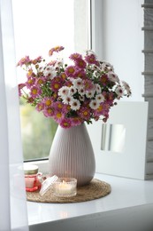 Photo of Beautiful flowers in vase and candles near window at home