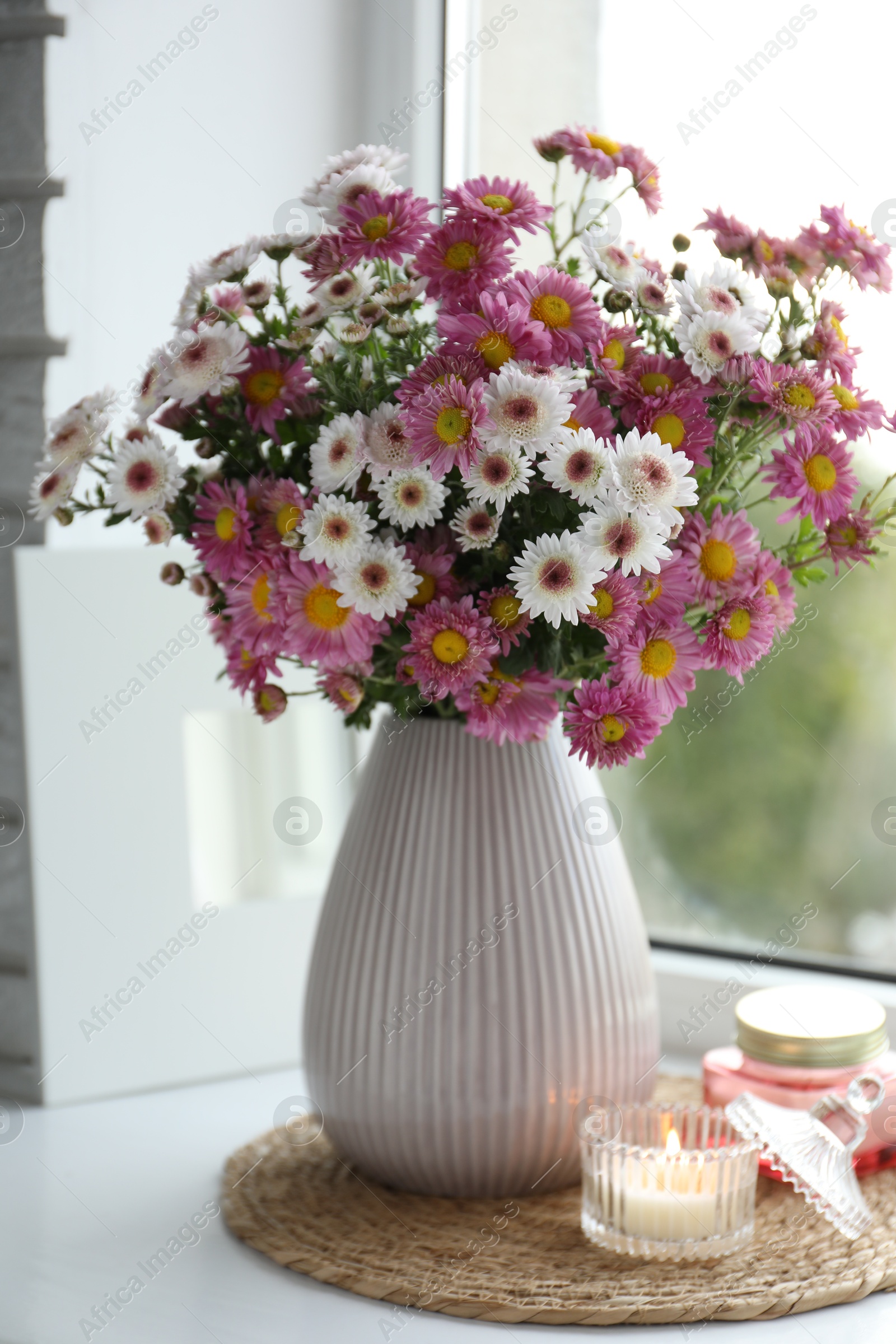 Photo of Beautiful flowers in vase and candles near window at home