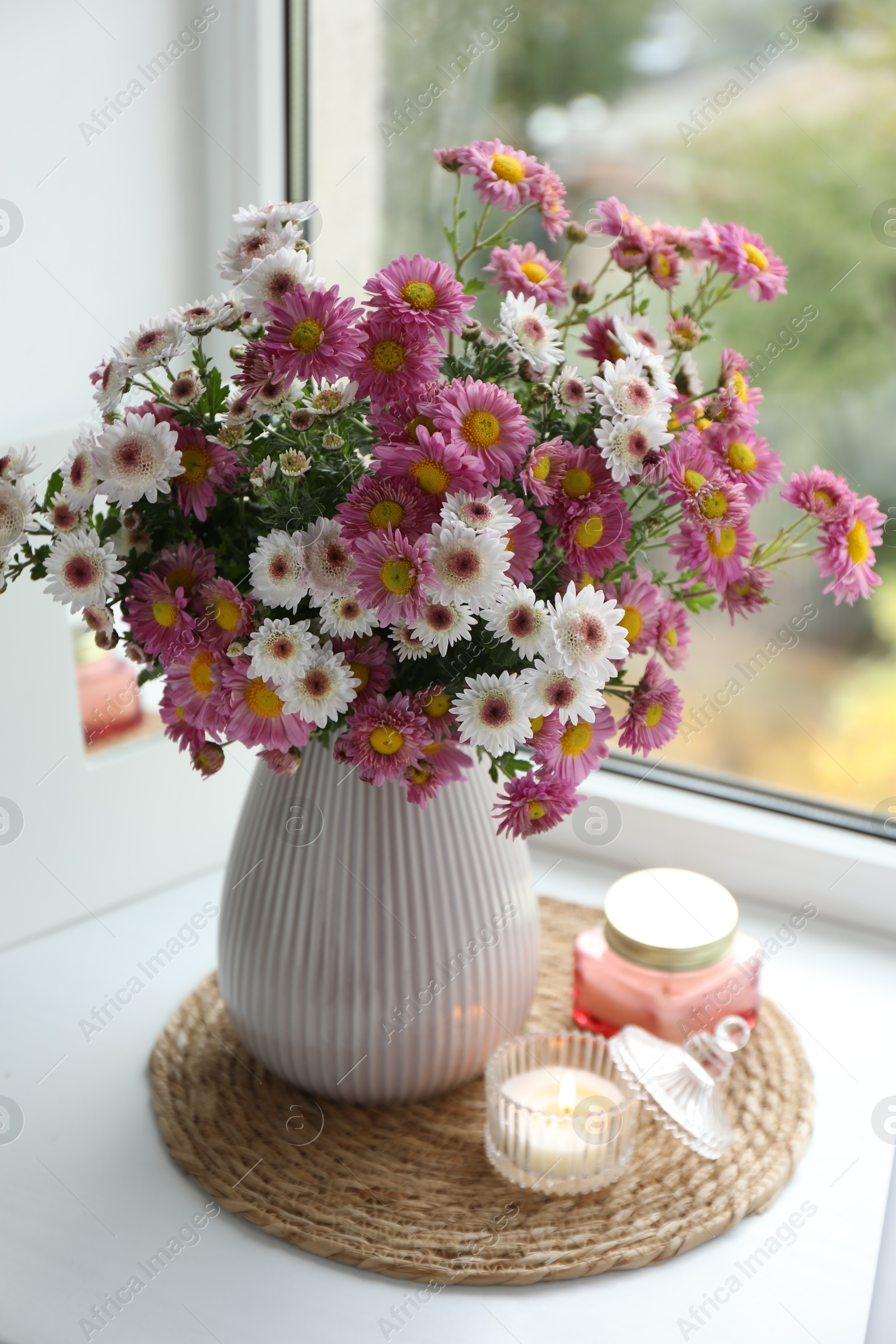 Photo of Beautiful flowers in vase and candles near window at home