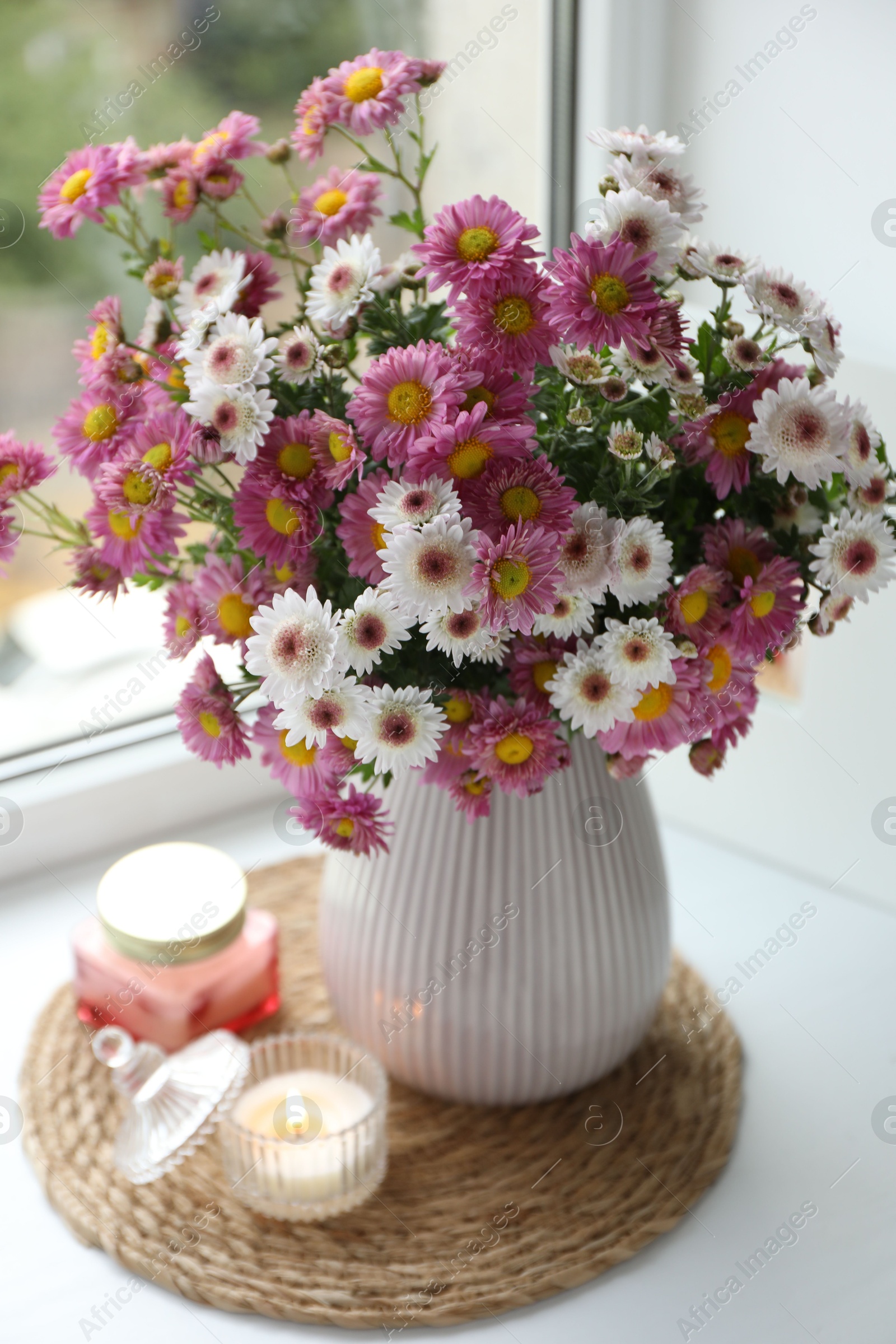 Photo of Beautiful flowers in vase and candles near window at home