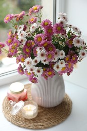 Photo of Beautiful flowers in vase and candles near window at home