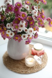 Photo of Beautiful flowers in vase and candles near window at home