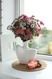 Photo of Stylish vase with beautiful flowers and burning candle near window at home