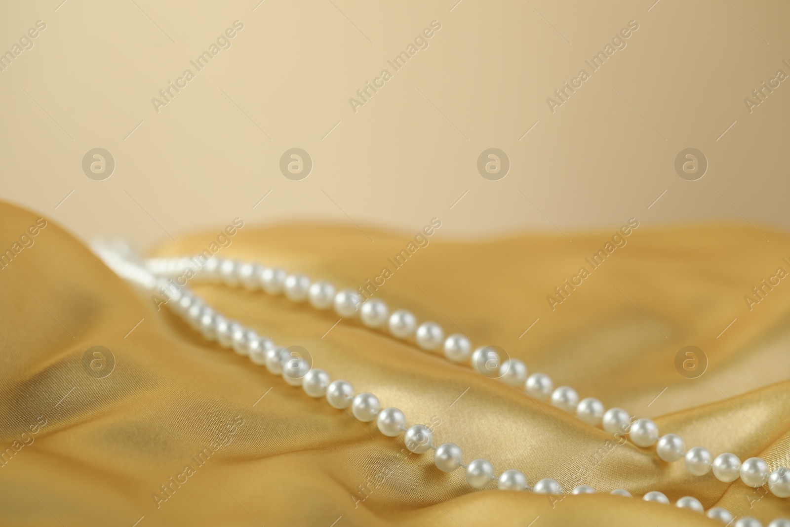 Photo of Beautiful pearl necklace on golden silk, closeup. Space for text