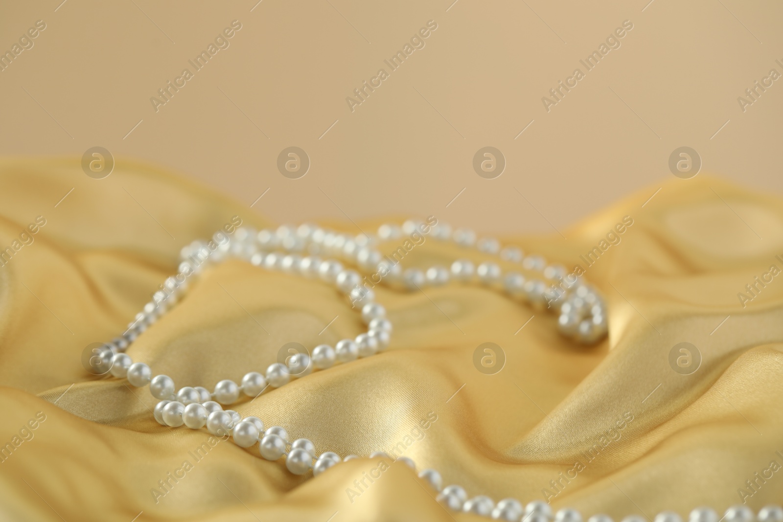 Photo of Beautiful pearl necklace on golden silk, closeup