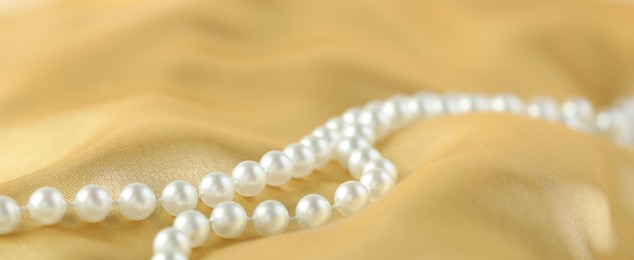 Photo of Beautiful pearl necklace on golden silk, closeup