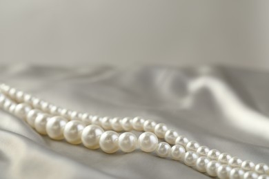 Photo of Beautiful pearl necklace on white silk, closeup. Space for text