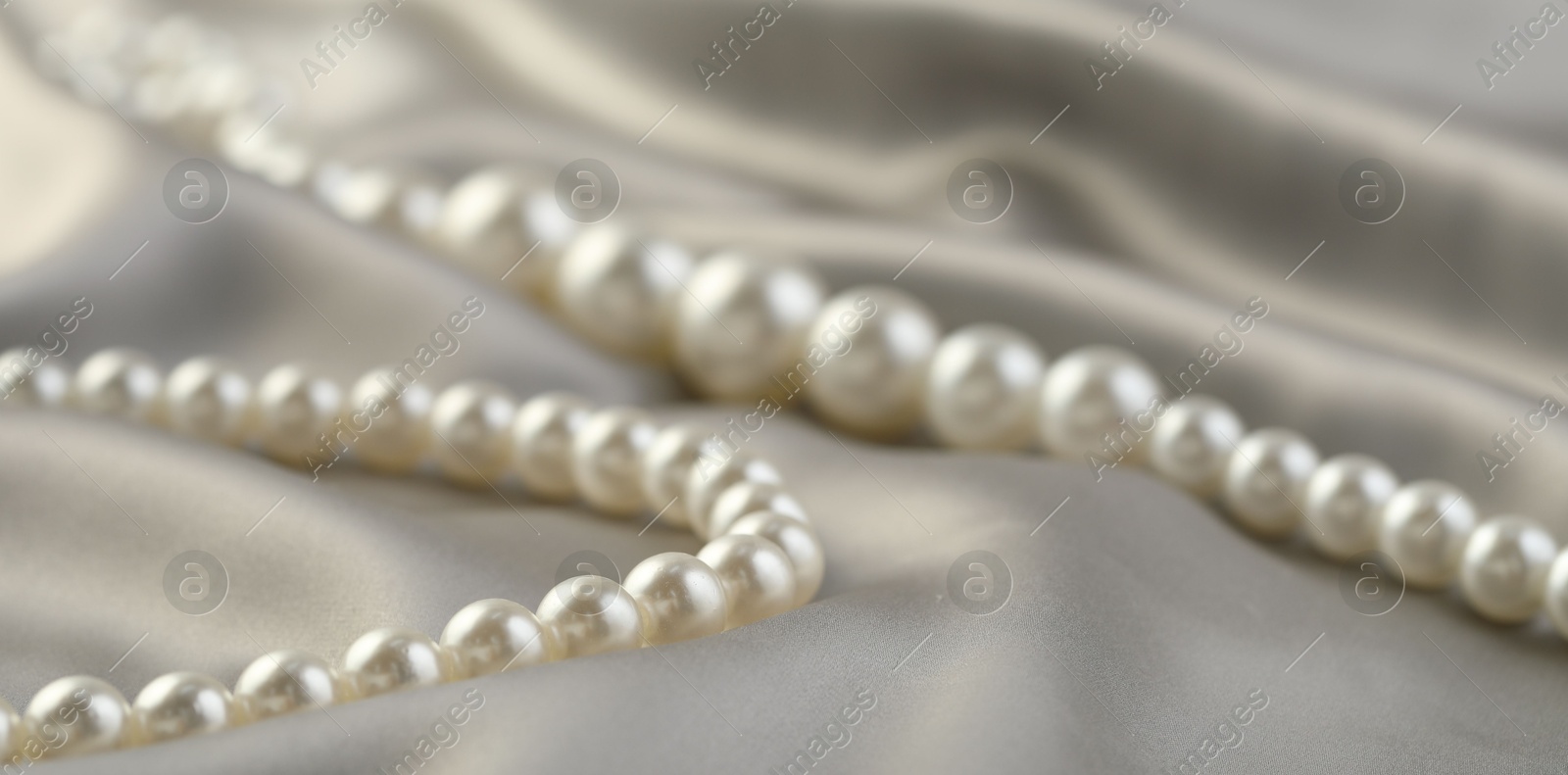 Photo of Beautiful pearl necklace on white silk, closeup