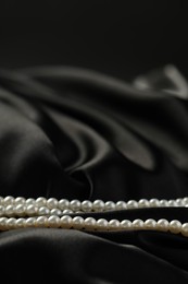 Photo of Beautiful pearl necklace on black silk, closeup. Space for text