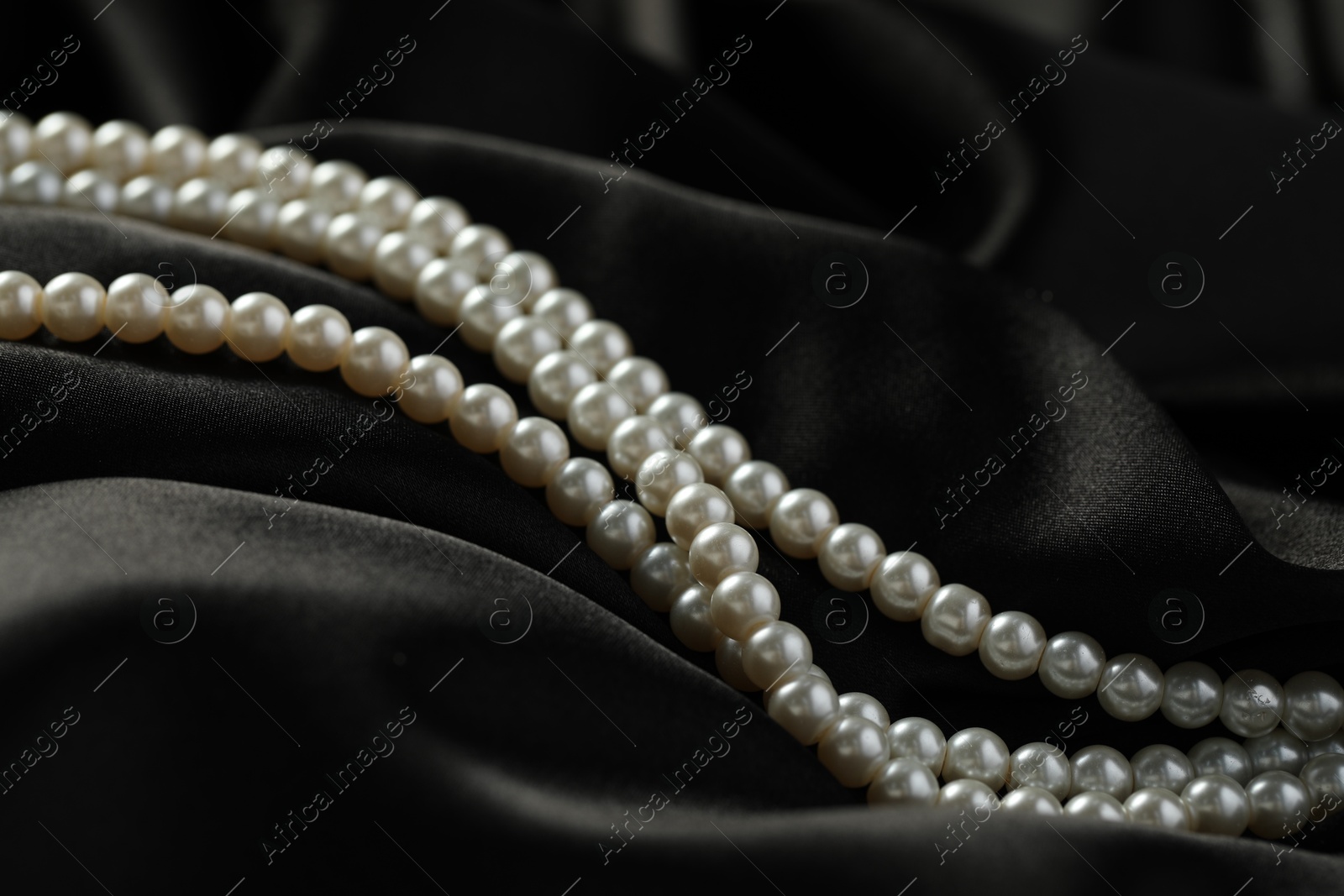 Photo of Beautiful pearl necklace on black silk, closeup