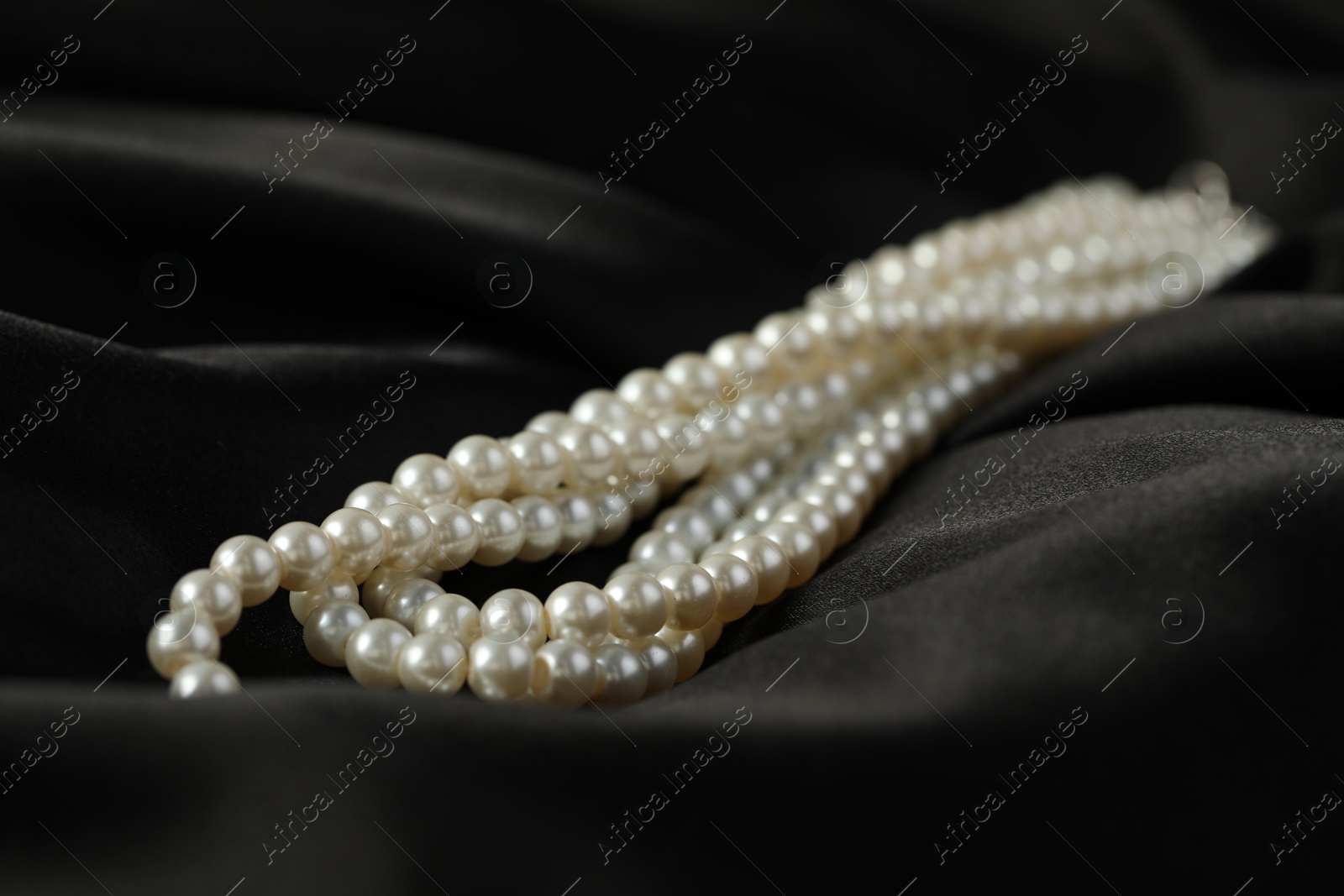 Photo of Beautiful pearl necklace on black silk, closeup