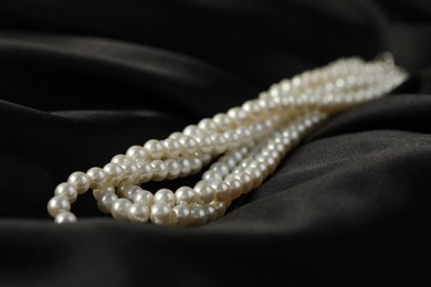 Photo of Beautiful pearl necklace on black silk, closeup