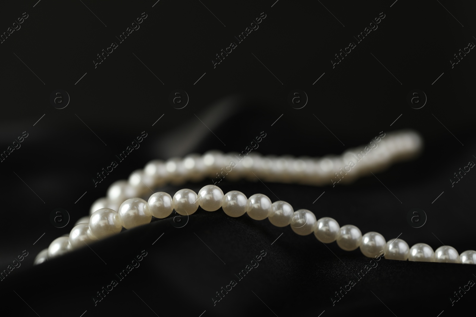 Photo of Beautiful pearl necklace on black silk, closeup