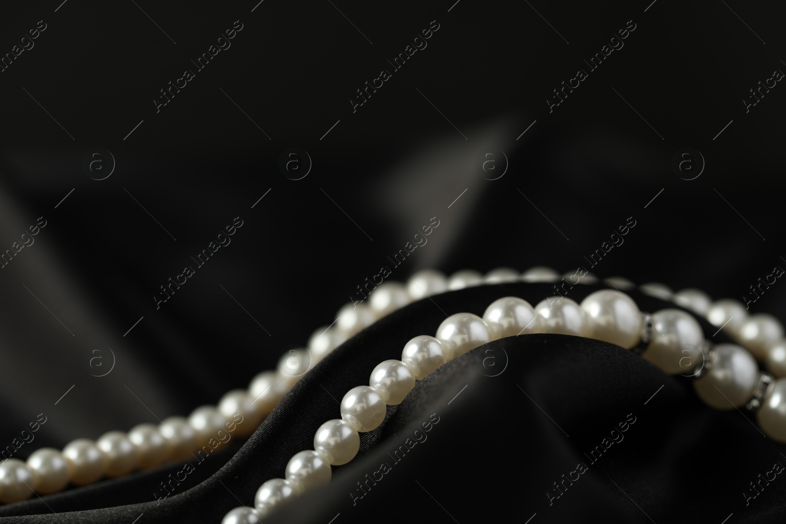 Photo of Beautiful pearl necklace on black silk, closeup