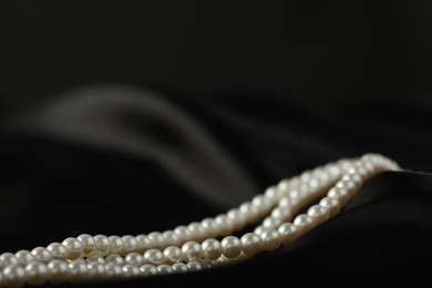 Photo of Beautiful pearl necklace on black silk, closeup. Space for text