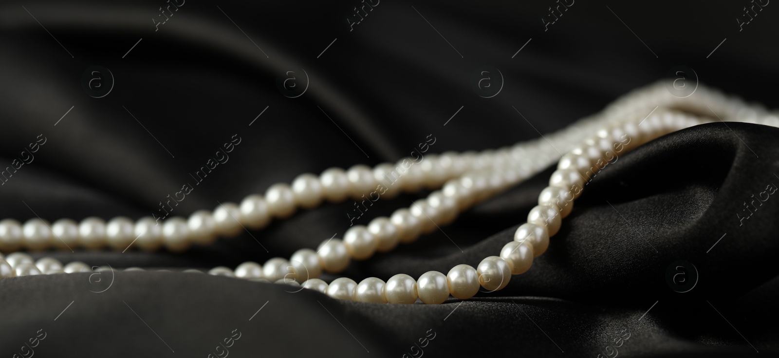 Photo of Beautiful pearl necklace on black silk, closeup