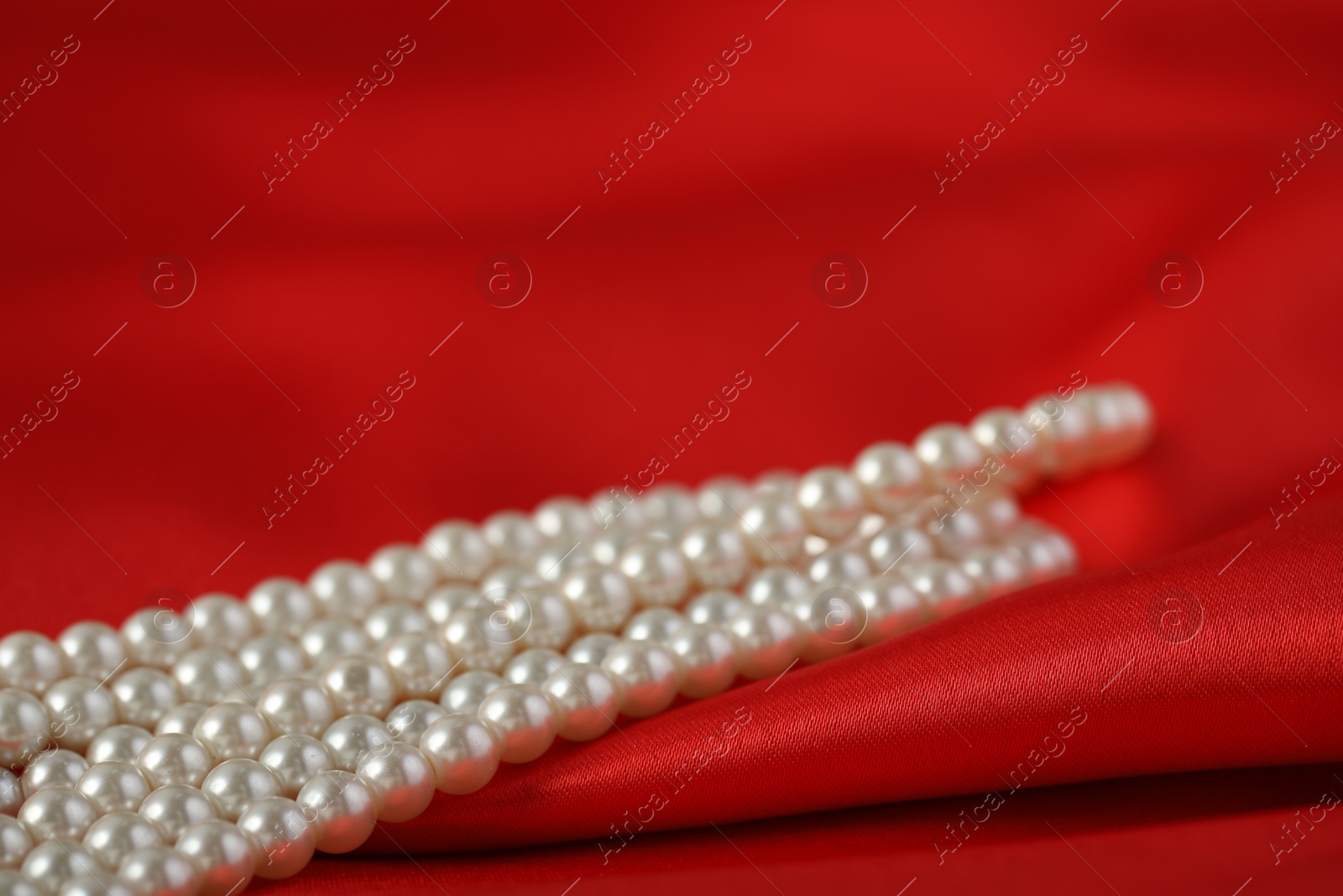 Photo of Beautiful pearl necklace on red silk, closeup. Space for text