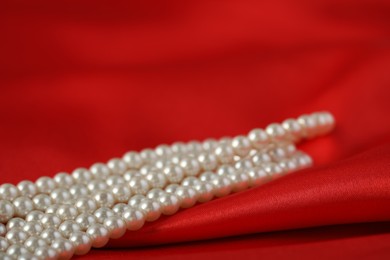 Photo of Beautiful pearl necklace on red silk, closeup. Space for text