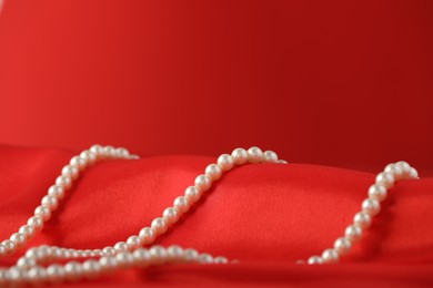 Photo of Beautiful pearl necklace on red silk, closeup. Space for text