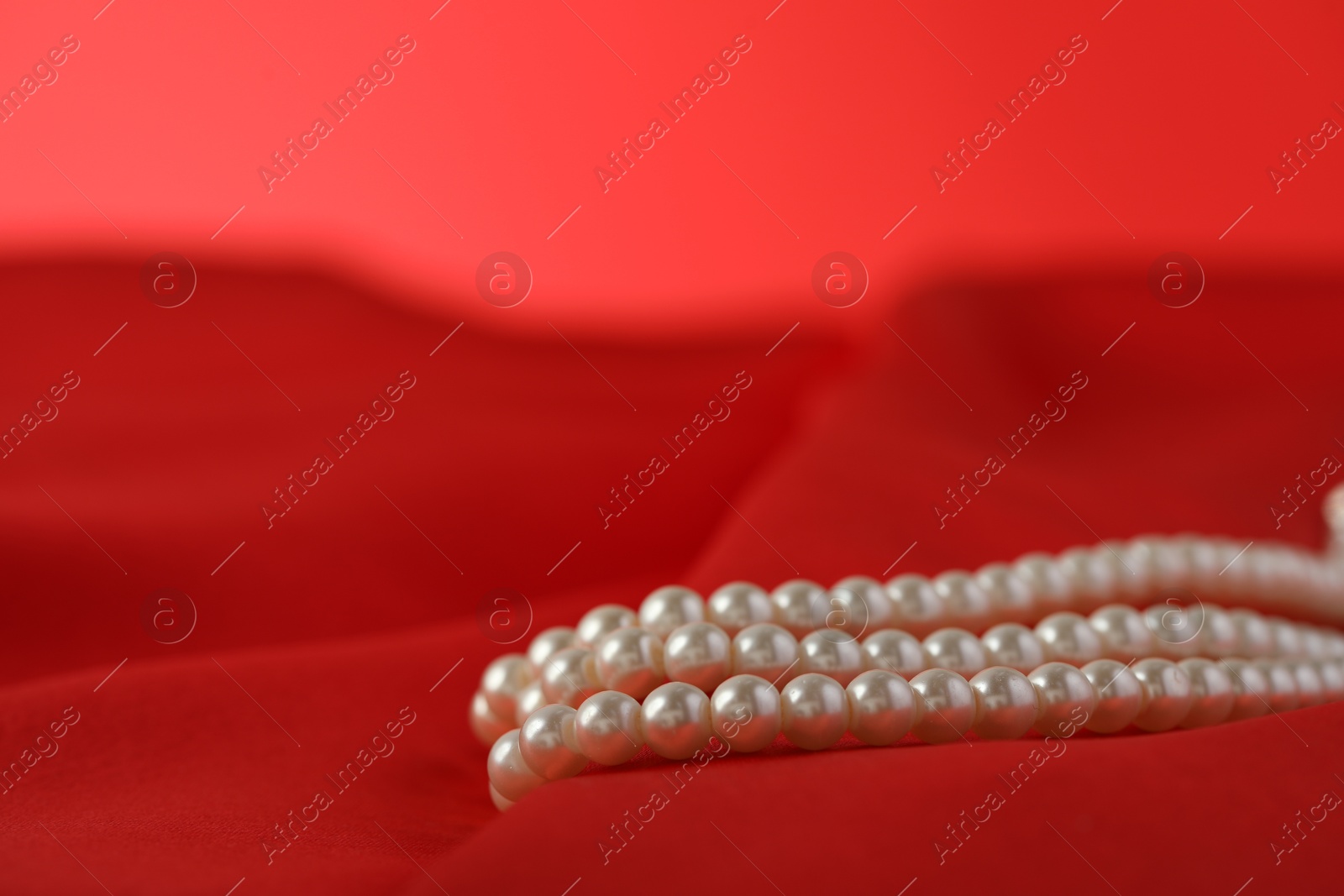 Photo of Beautiful pearl necklace on red silk, closeup. Space for text