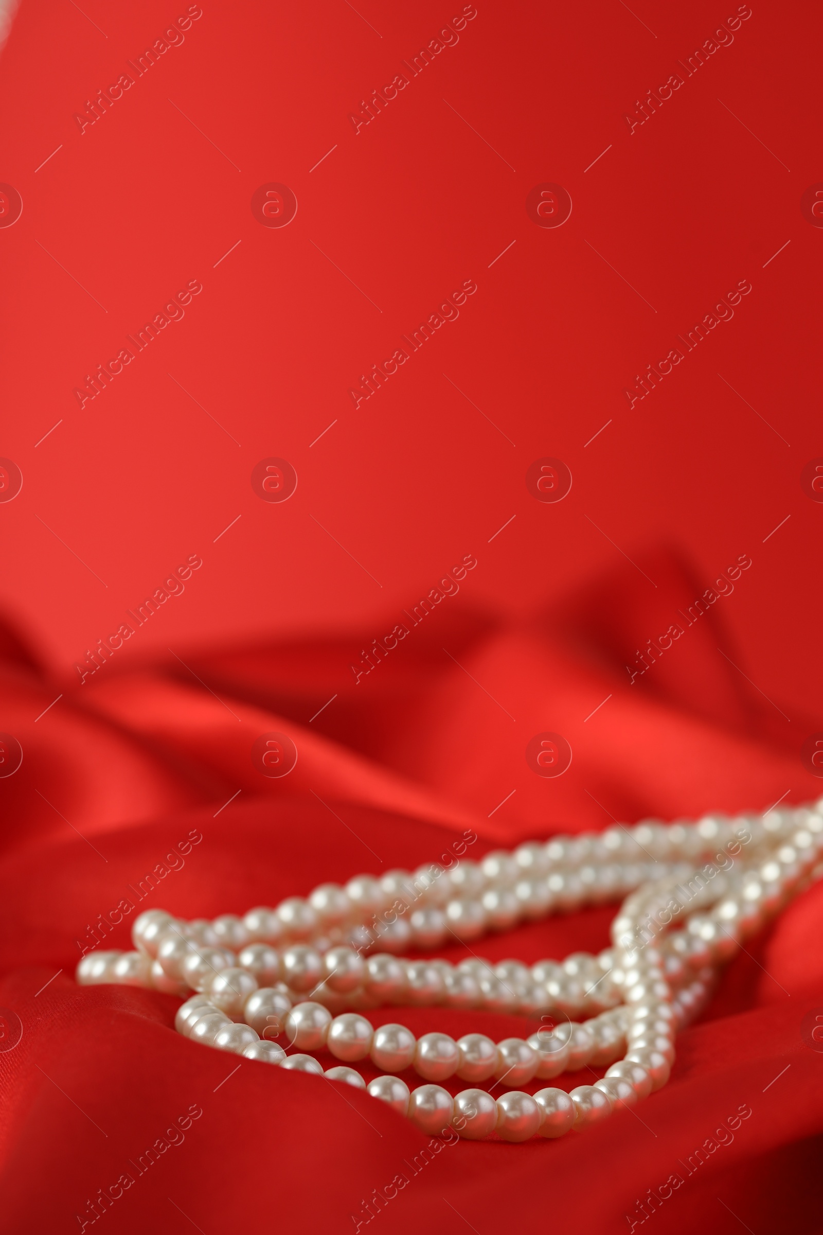 Photo of Beautiful pearl necklace on red silk, closeup. Space for text