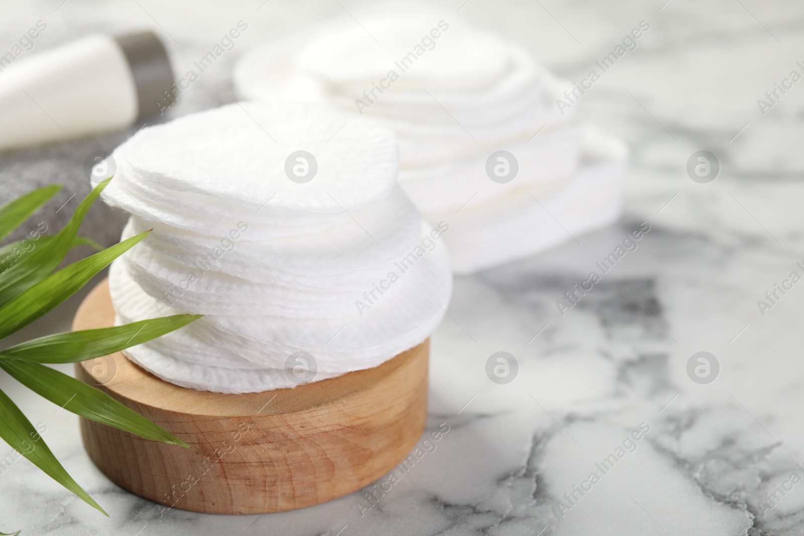 Photo of Cotton pads and palm leaf on light marble table, closeup