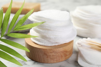 Photo of Cotton pads, swabs and palm leaf on light marble table, closeup