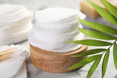 Photo of Cotton pads, swabs and palm leaf on light marble table, closeup