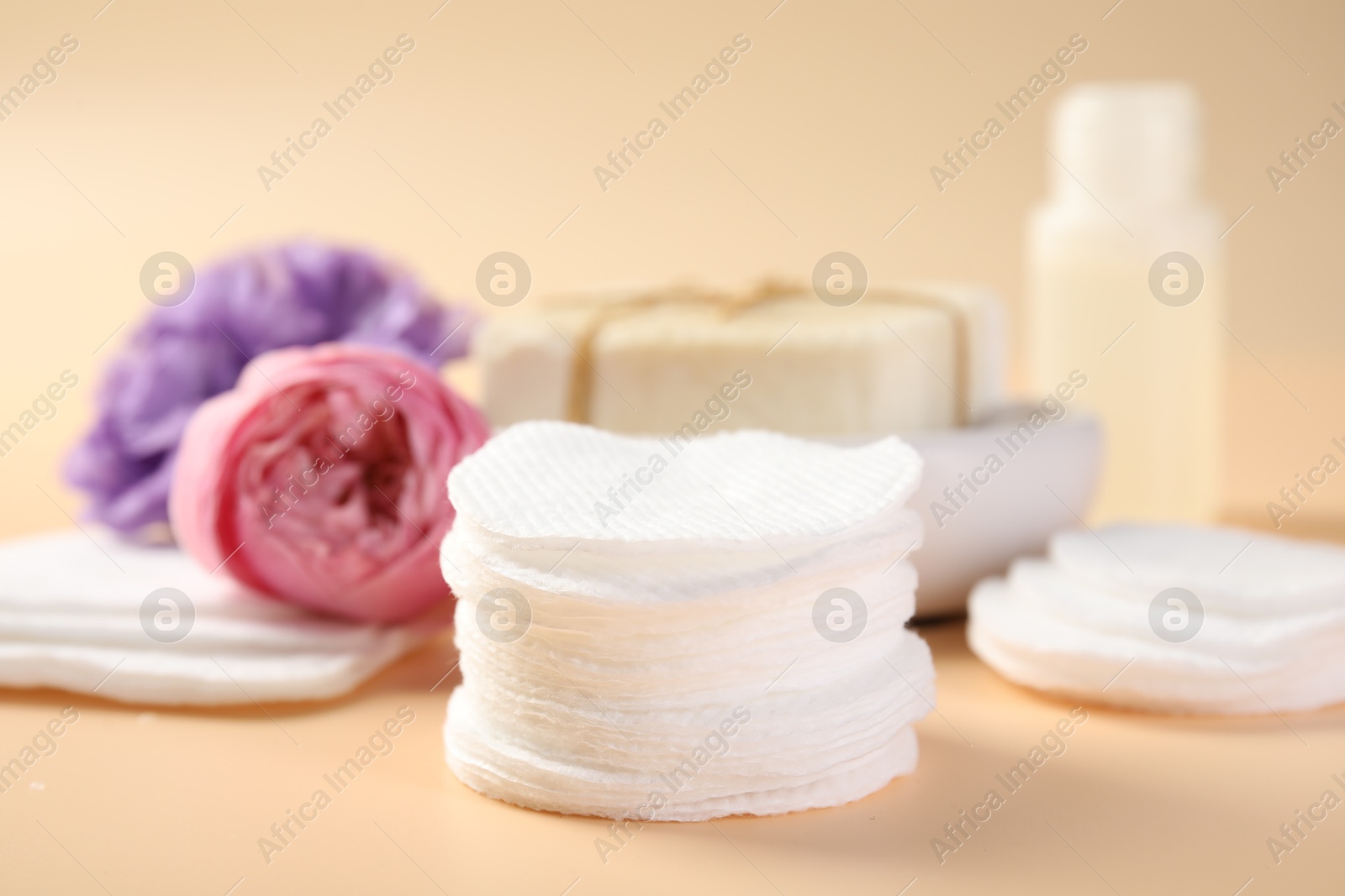 Photo of Cotton pads, cosmetic products and flowers on beige background, closeup