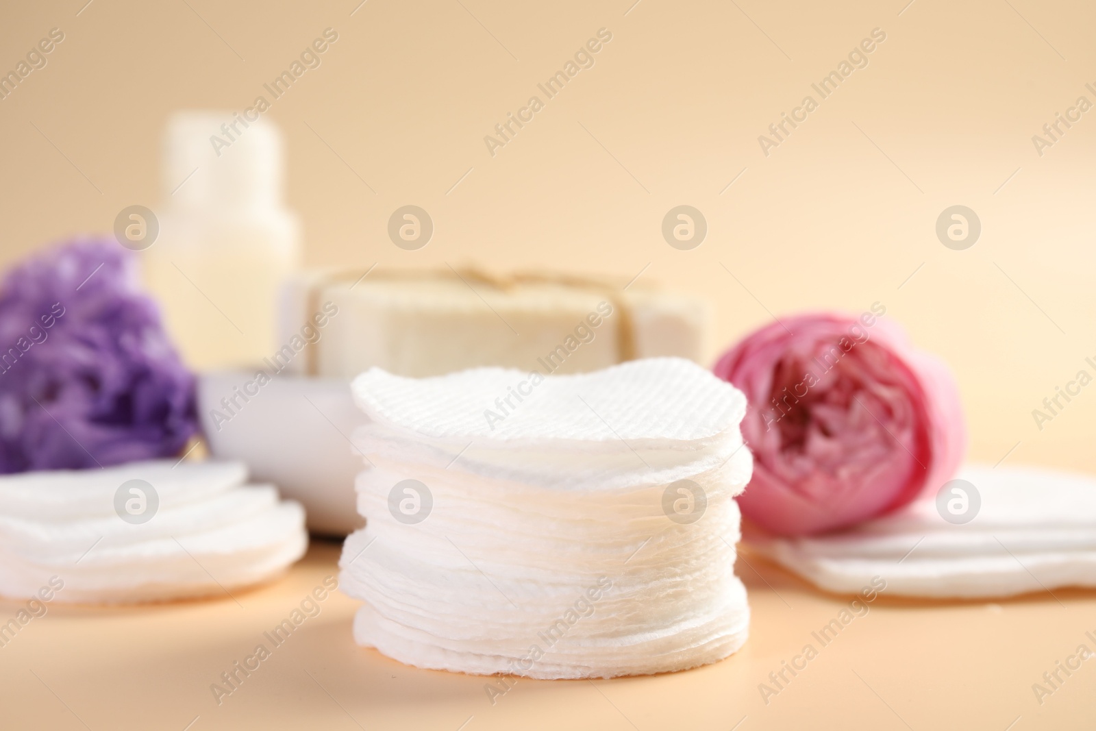 Photo of Cotton pads, cosmetic products and flowers on beige background, closeup