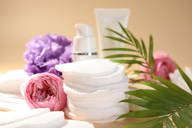 Photo of Cotton pads, cosmetic products, flowers and palm leaves on beige background, closeup