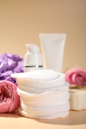 Photo of Cotton pads, cosmetic products and flowers on beige background, closeup