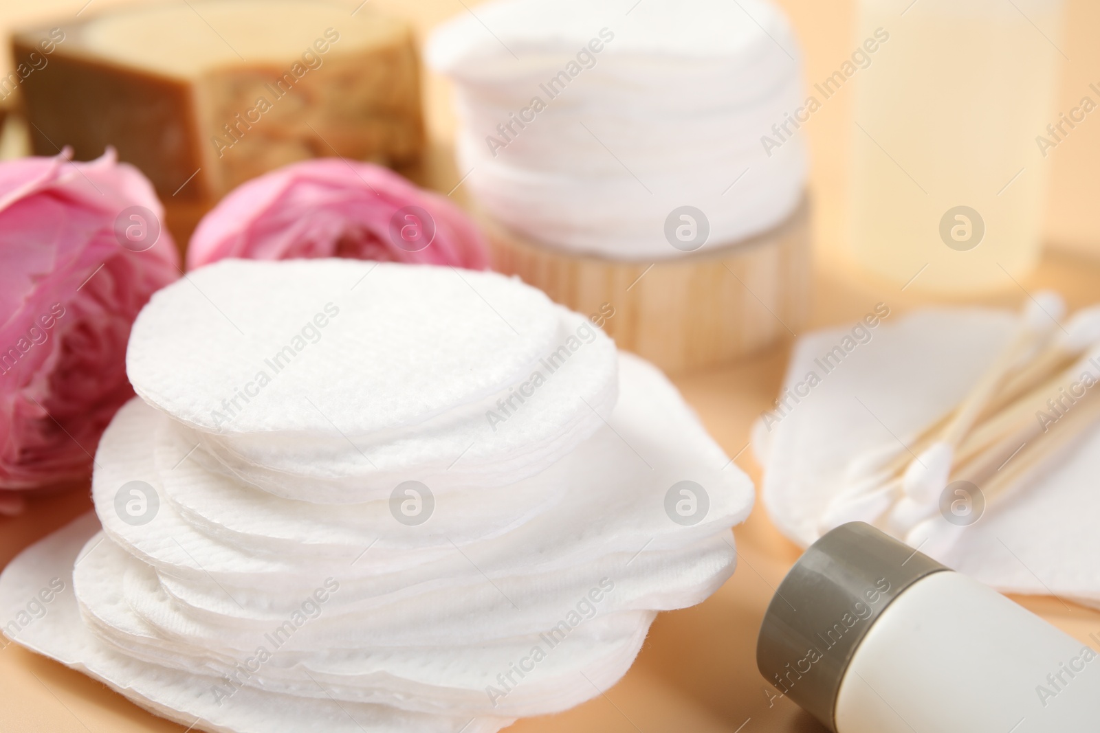 Photo of Cotton pads, cosmetic products, swabs and flowers on beige background, closeup