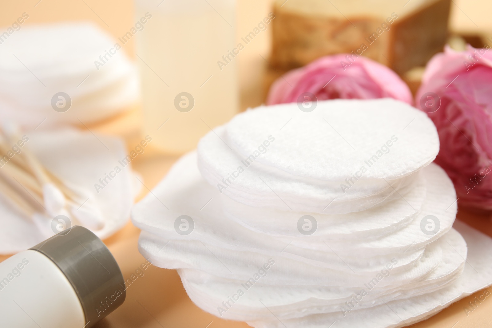 Photo of Cotton pads, cosmetic products, swabs and flowers on beige background, closeup