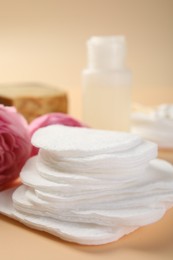 Photo of Cotton pads, cosmetic products and flowers on beige background, closeup