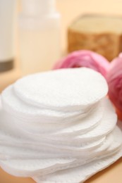 Photo of Cotton pads, cosmetic products and flowers on beige background, closeup